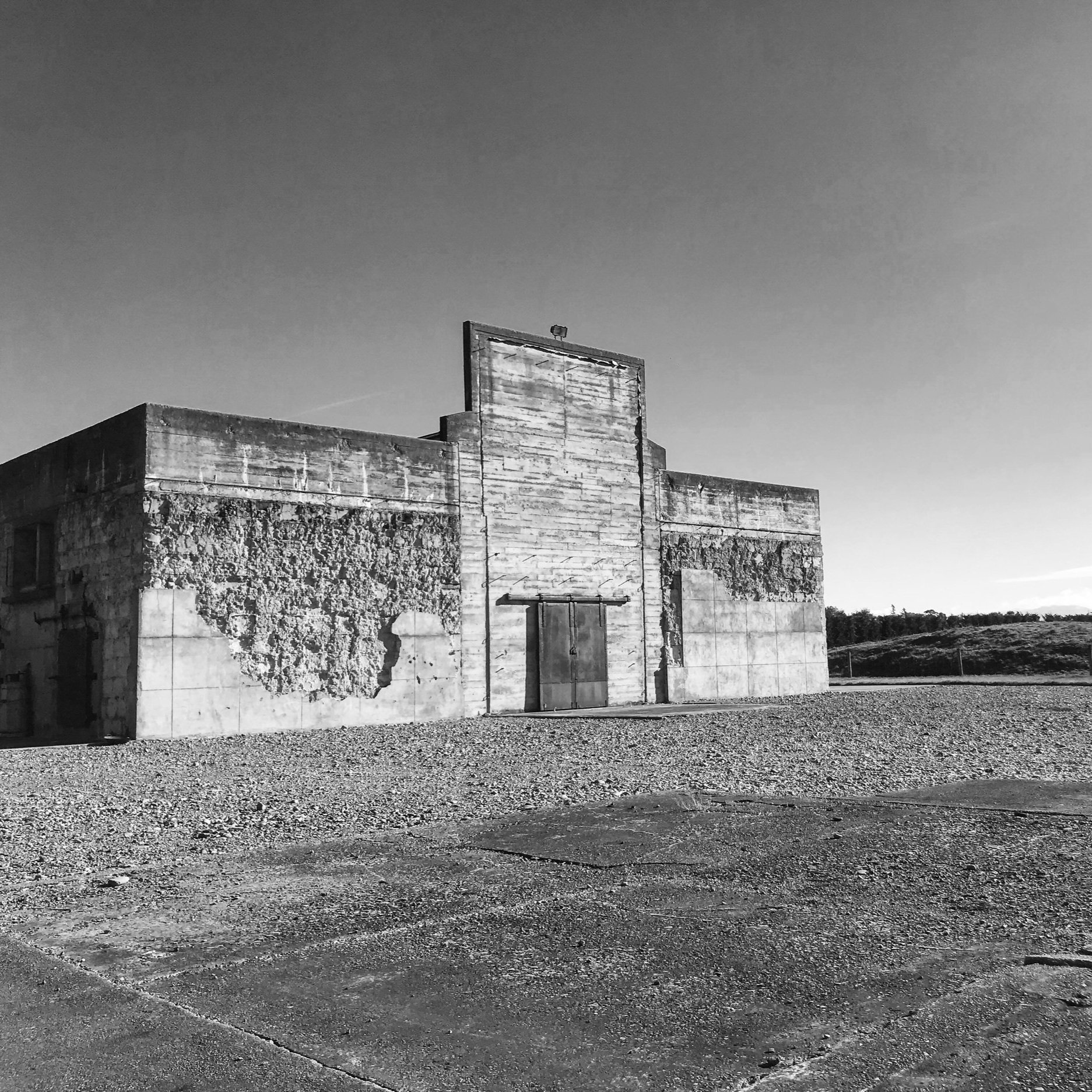 Weathered concrete block building with recessed door, open gravel surrounds