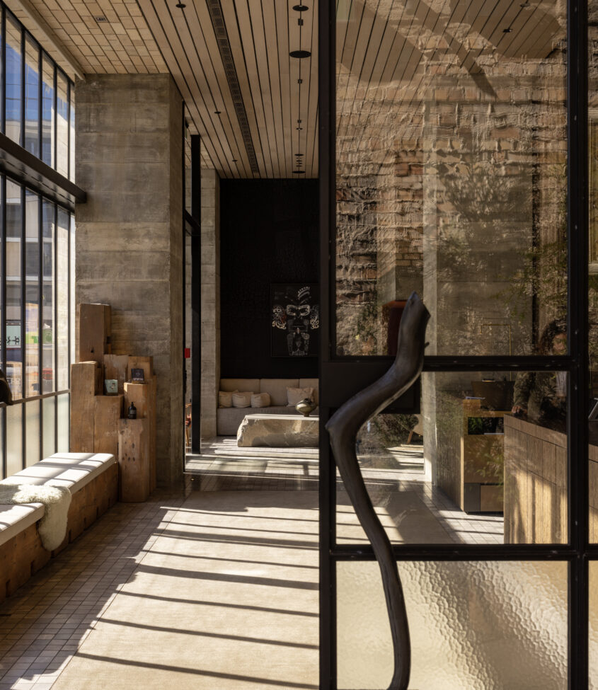 Raw concrete and timber interior with black steel-frame windows, stone bench seating and sculpture