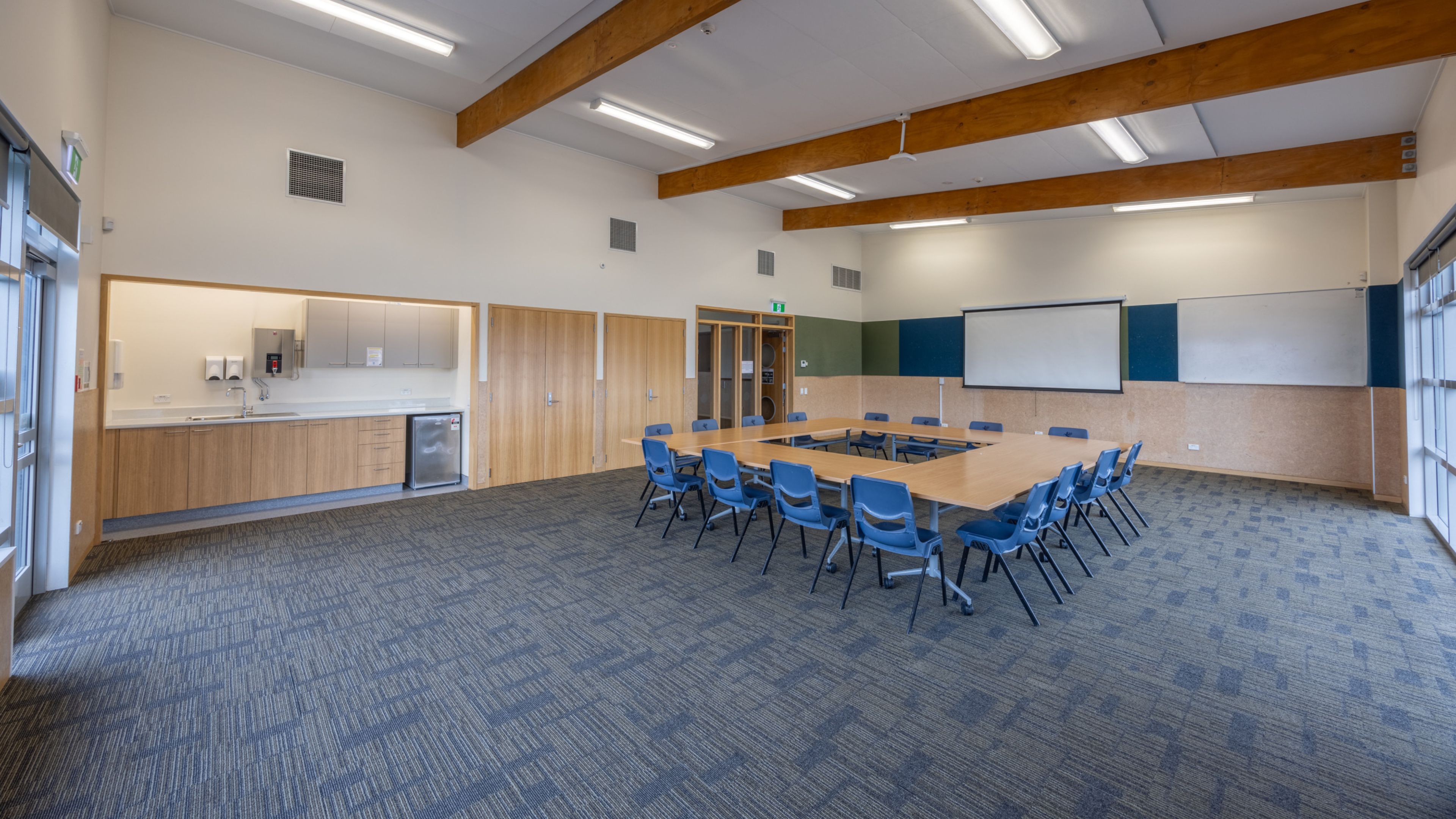 Community hall with exposed timber beams, tables in U-shape arrangement and whiteboard