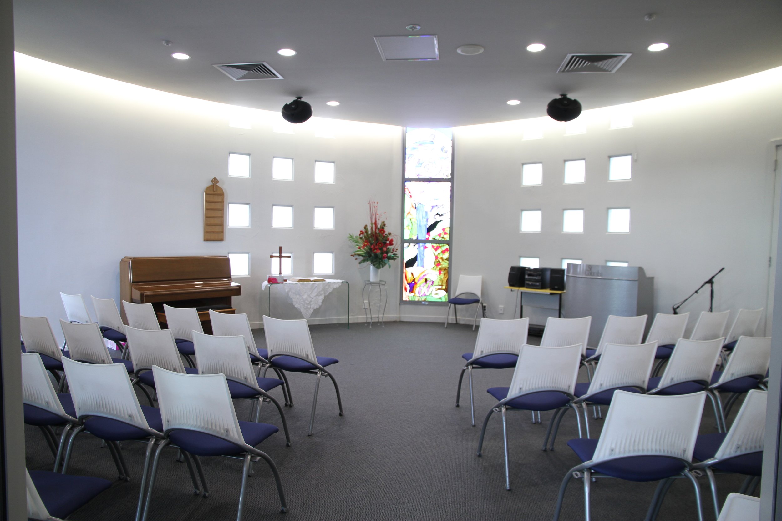 Oval chapel with curved walls, stained glass window and white seating