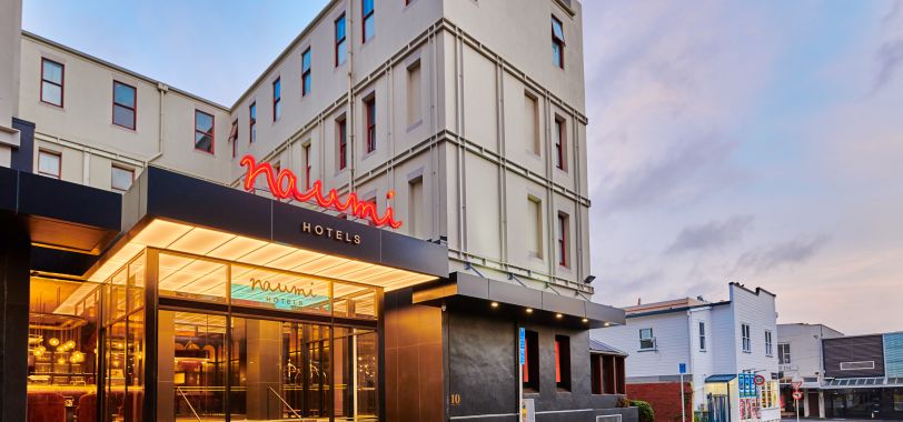 Cream multi-storey building with black canopy entrance, neon signage, street setting at dusk