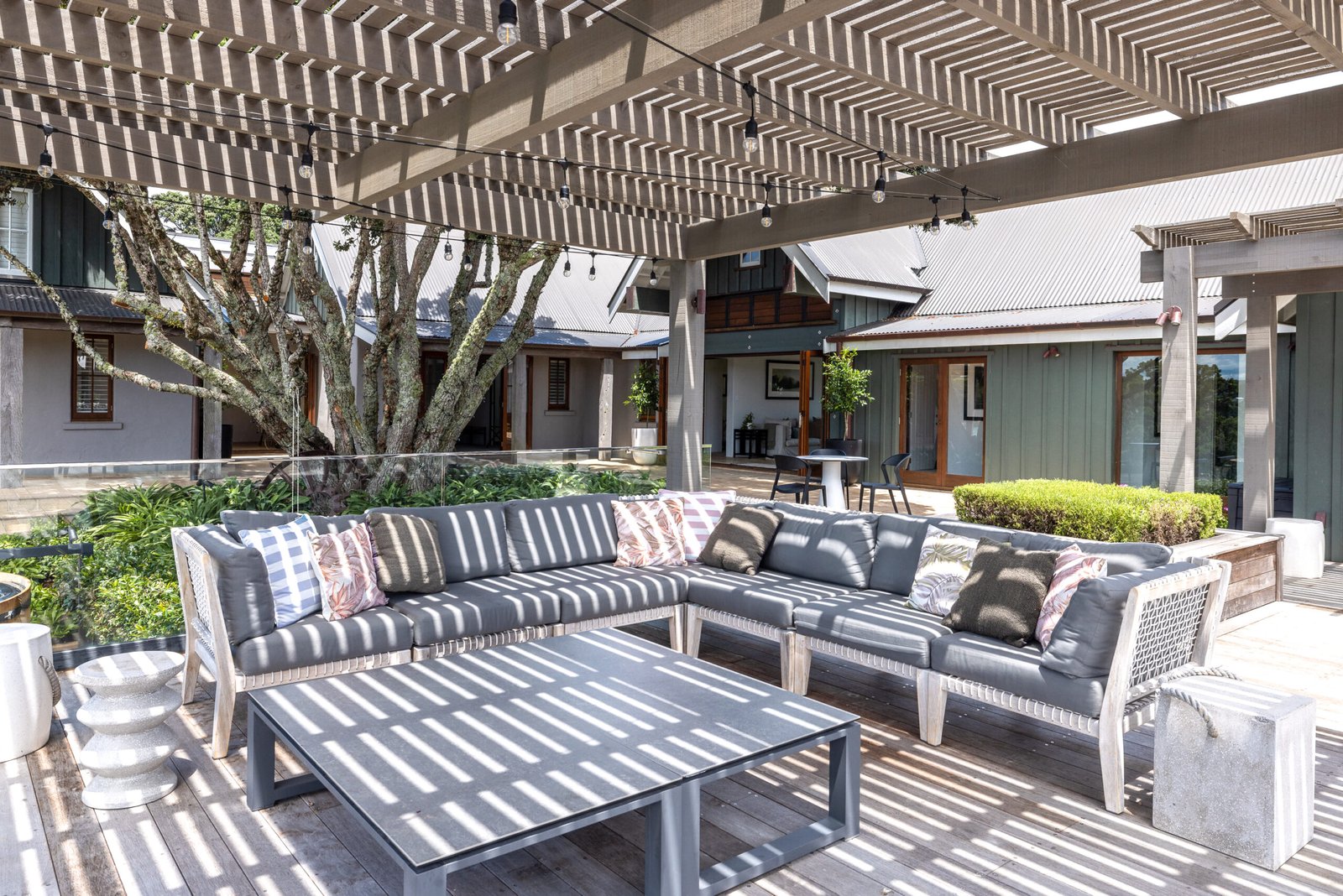 Covered outdoor terrace with timber pergola, grey outdoor sofas and courtyard building surrounds