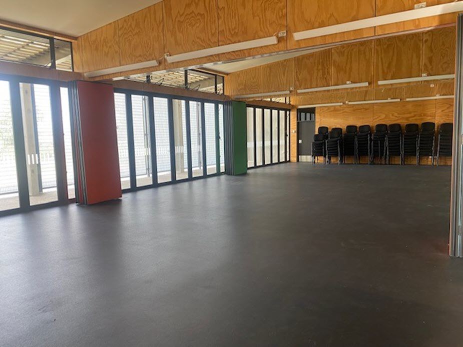 Large open hall with plywood-lined walls and stacked chairs along one side