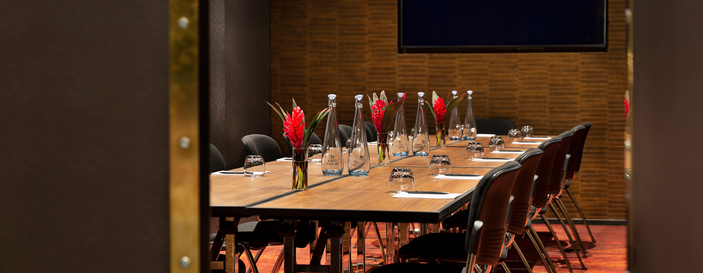 Dark timber-slat meeting room with black conference table, large screen, and long windows