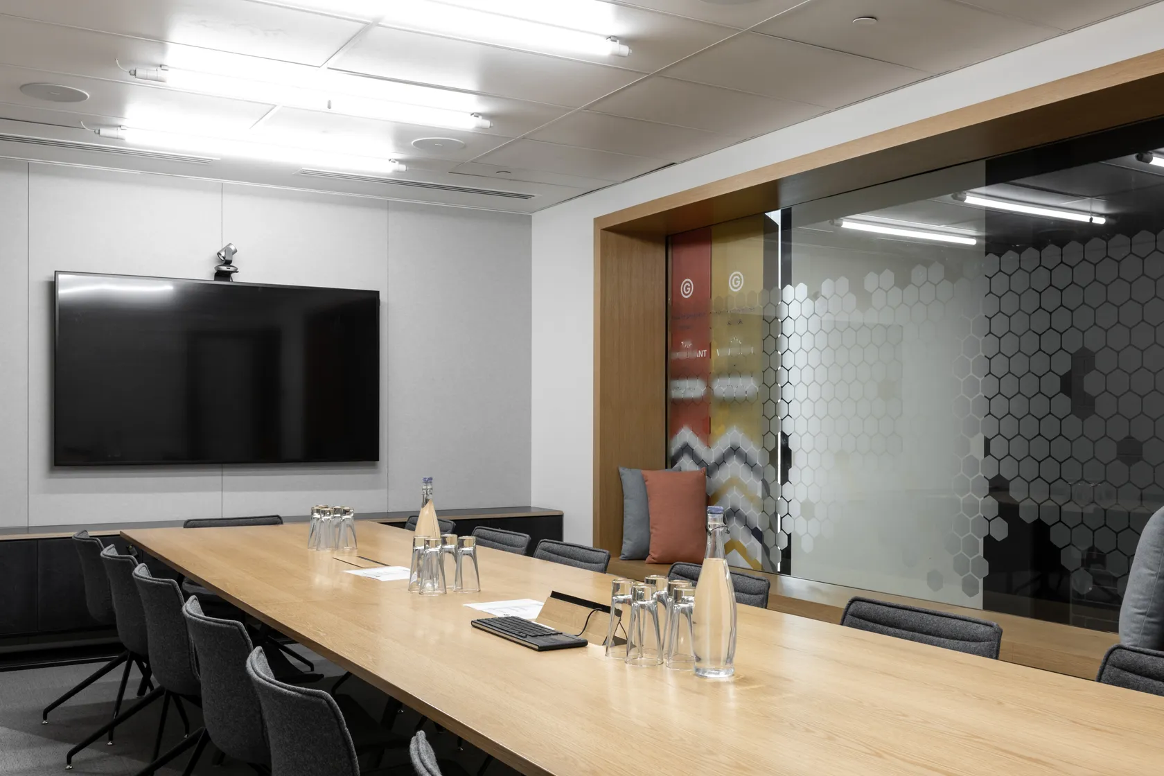 Boardroom with long timber table, chairs, large screen, and patterned glass partition