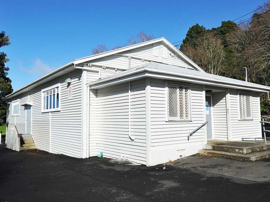 White-painted weatherboard hall building with steps and trees behind