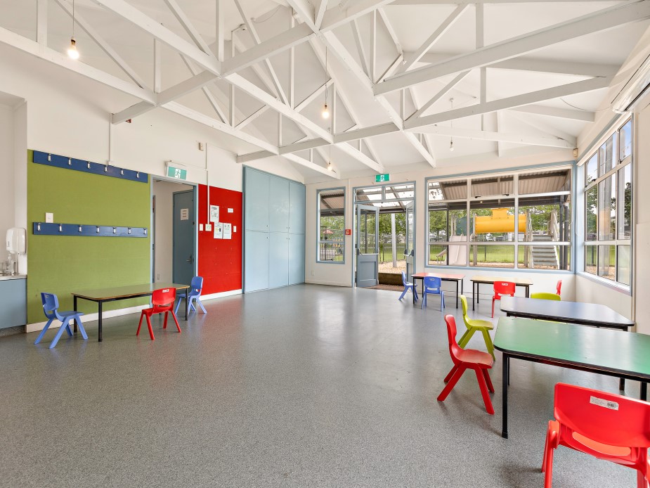 Bright hall with exposed roof trusses, coloured walls and small chairs