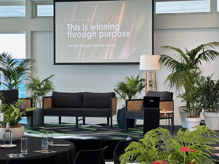 Function room set for a conference with projection screen, sofa seating area, and potted plants