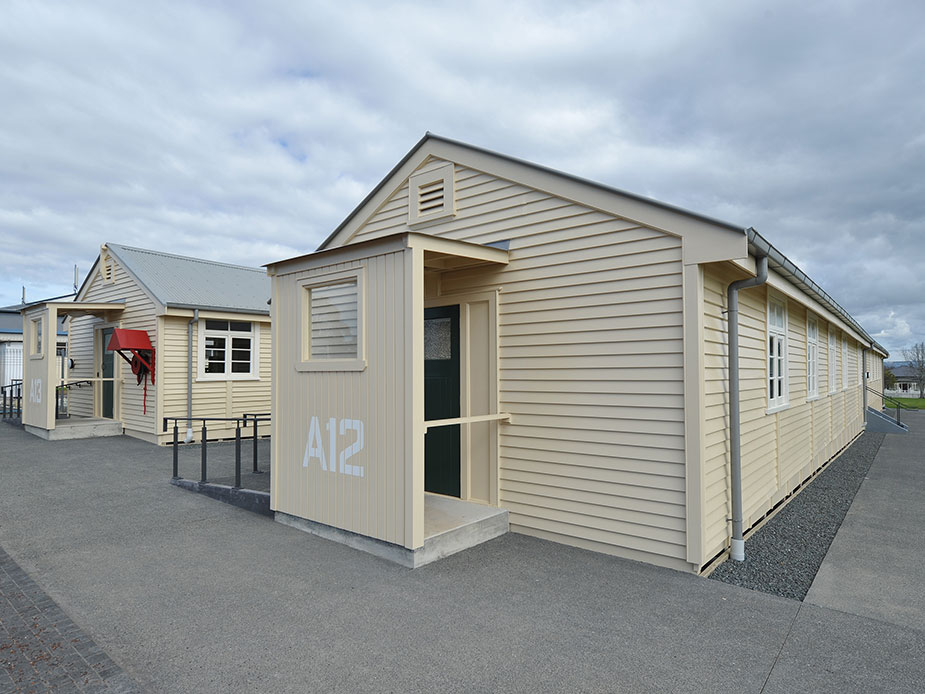 Single-storey cream weatherboard barrack buildings with 'A12' numbering