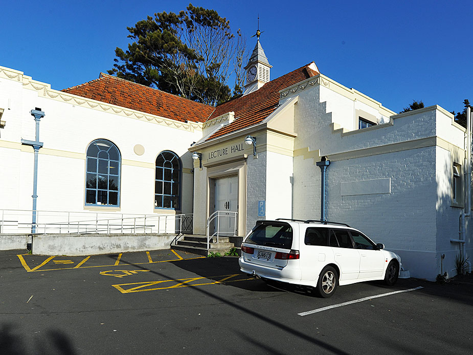 Lecture hall entrance with classical doorway and parked car in foreground