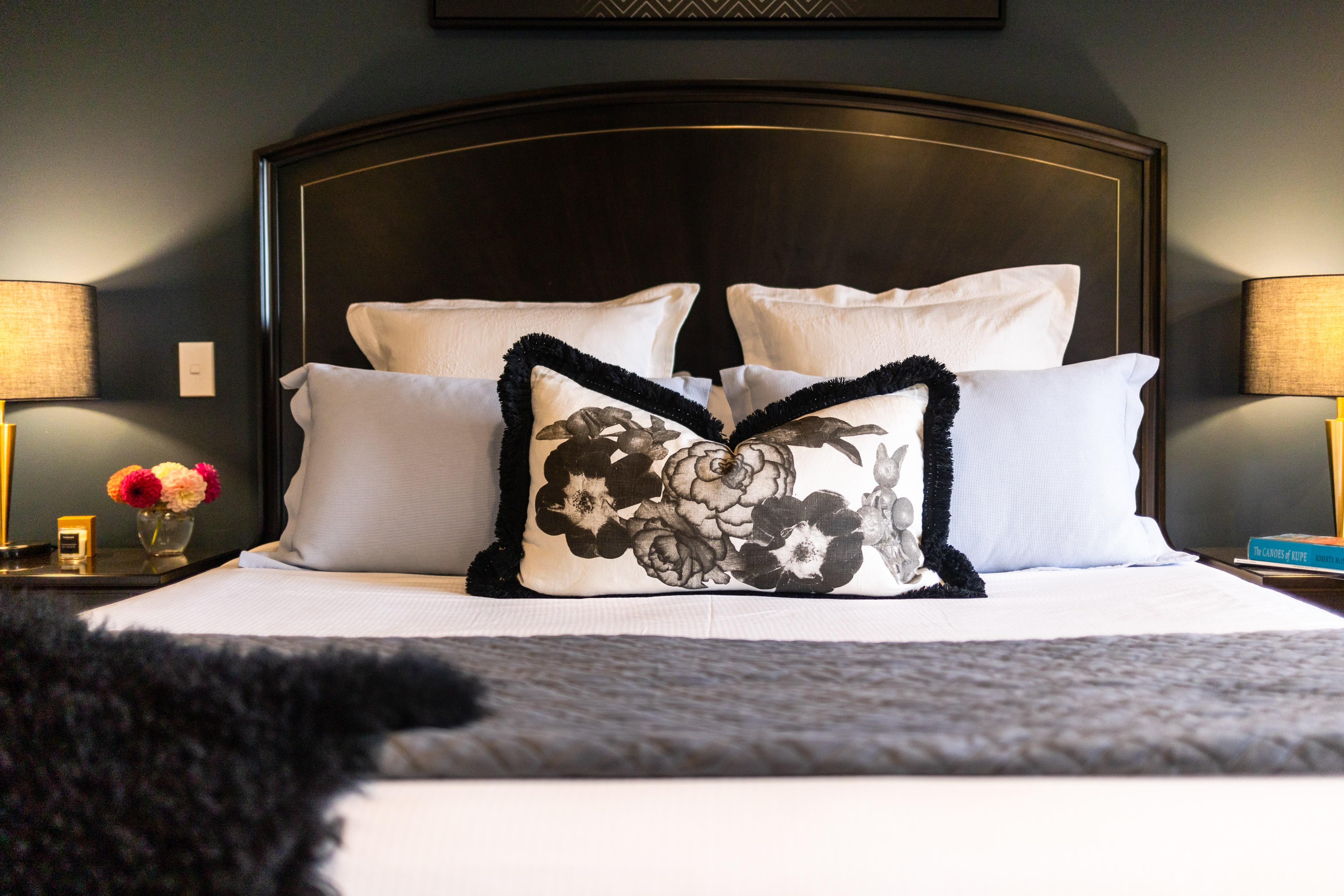 Dark-upholstered bed with floral cushion and bedside lamps, green-walled room