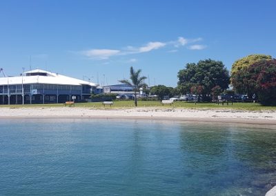 Club building viewed from water with beach and trees