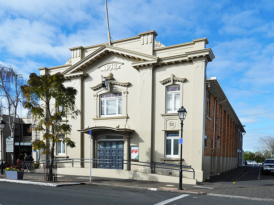 Cream rendered heritage hall with ornate parapet, arched entrance and columned porch, street corner