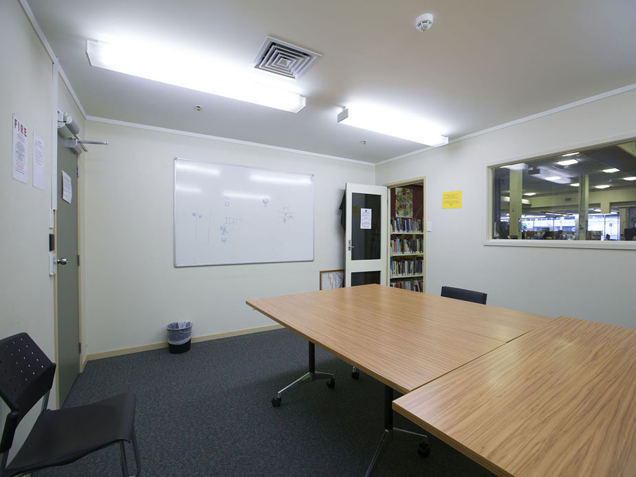 Small meeting room with timber table, whiteboard, and internal window to library