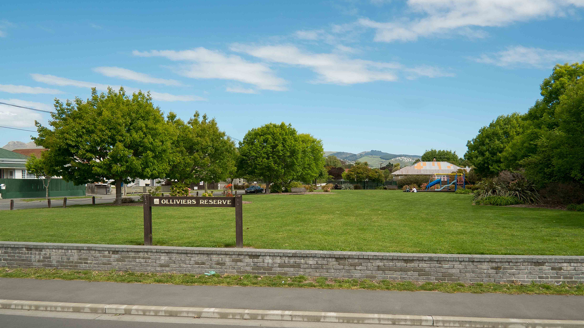 Open grassed reserve with trees and a playground in the background