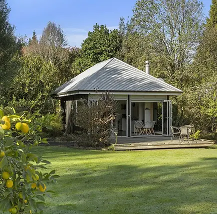 Small pavilion building with metal roof on a timber deck surrounded by garden