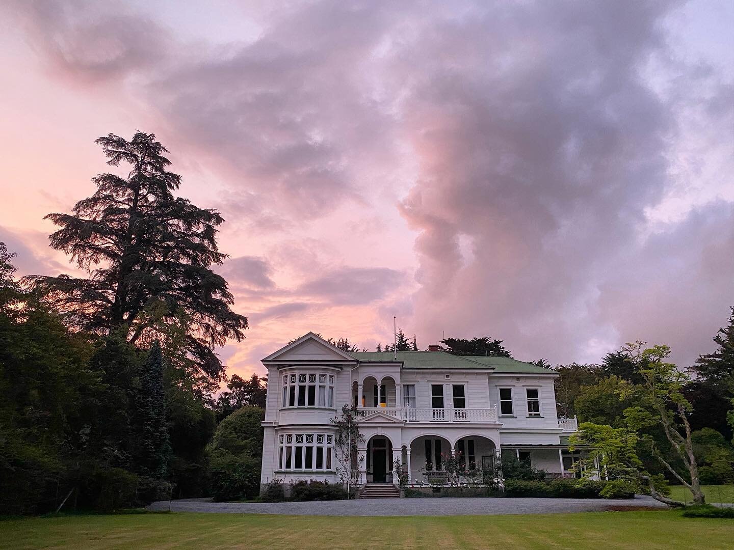 Two-storey white heritage homestead at dusk with dramatic pink sky