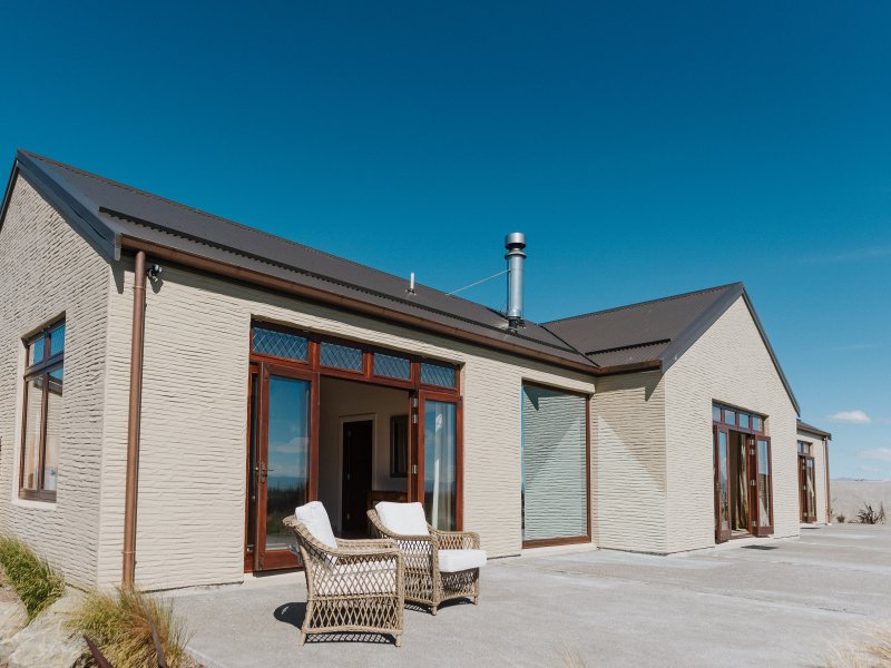 Cream render building with dark roof and timber-framed bi-fold doors, outdoor chairs on concrete patio