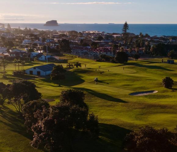 Aerial view of golf course fairways with coastal town and sea beyond