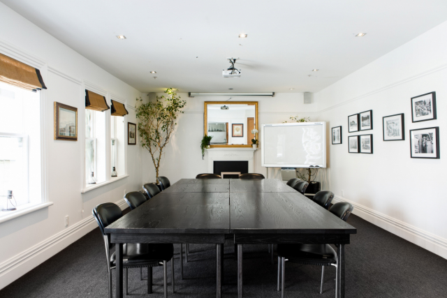 White-walled meeting room with long dark table, black chairs, fireplace and framed prints