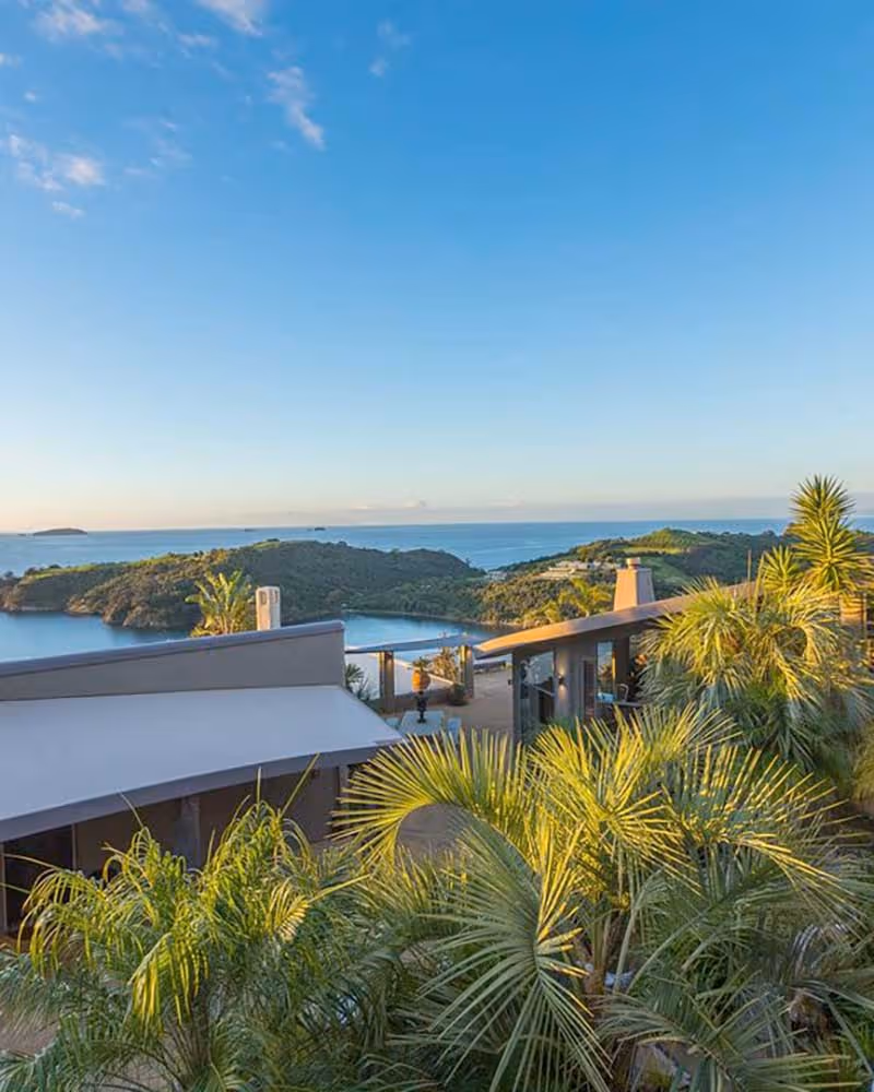 Low-profile contemporary building with flat overhanging roof amid dense tropical planting, water views and islands beyond