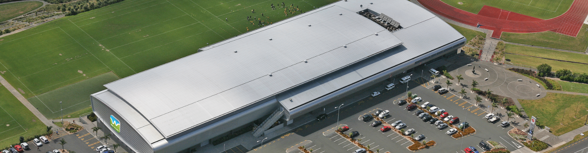 Aerial view of large indoor arena building with surrounding sports fields and car park