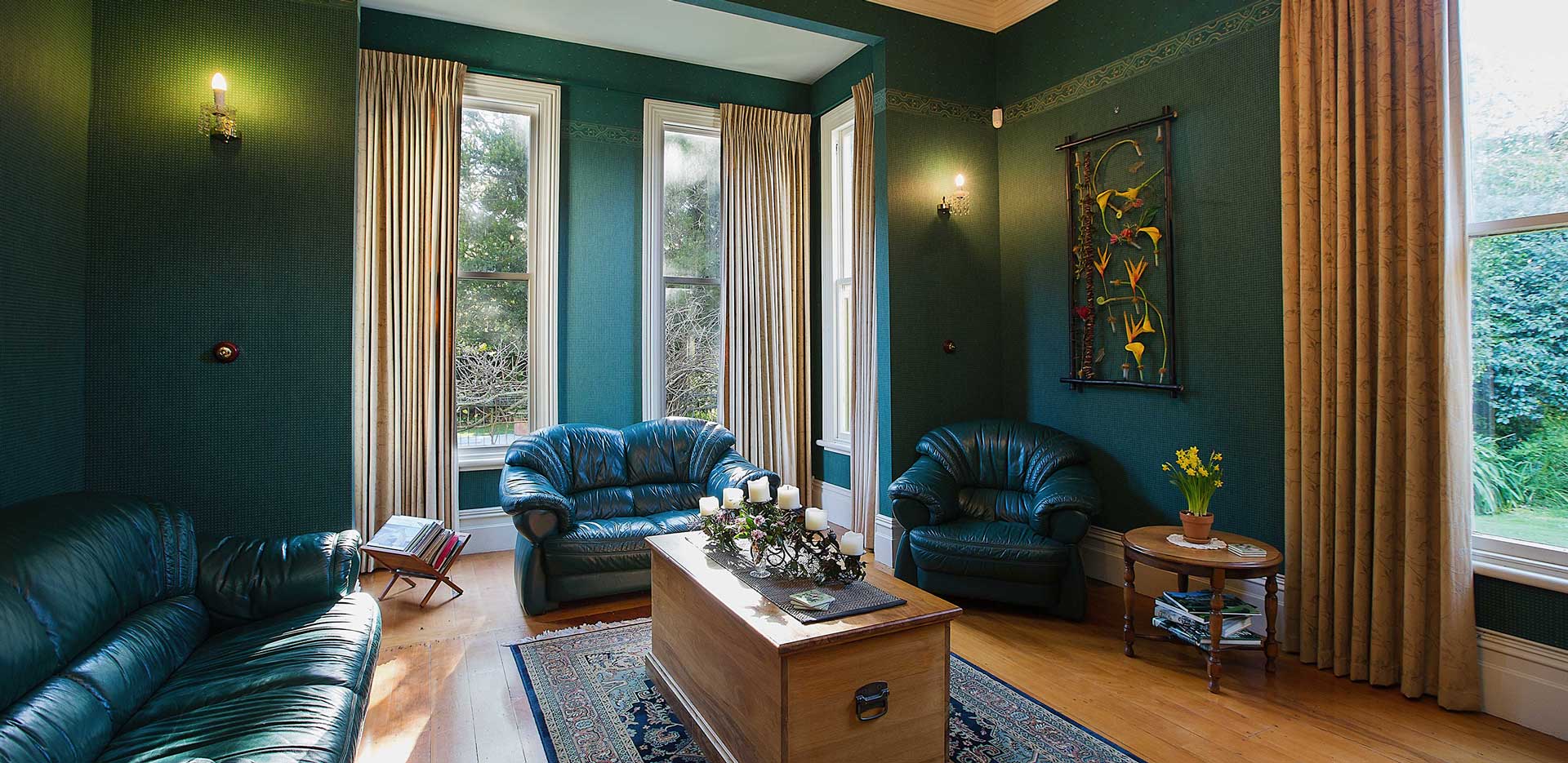 Sitting room with deep green walls, leather sofas, timber floor and tall sash windows