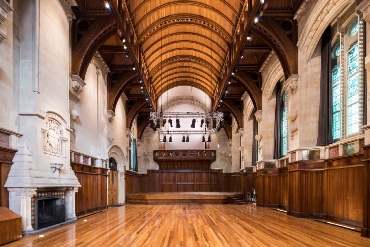 Grand hall with vaulted timber ceiling, stone arches, raised platform and polished floor