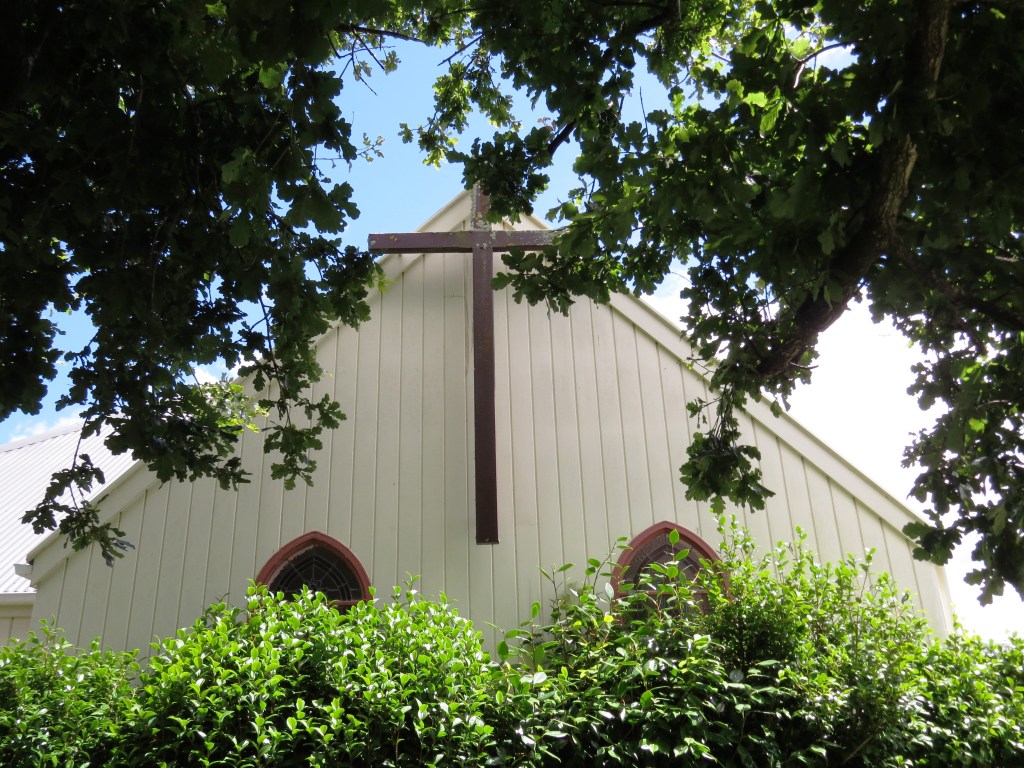 Church exterior with timber cross, arched windows and tree in foreground