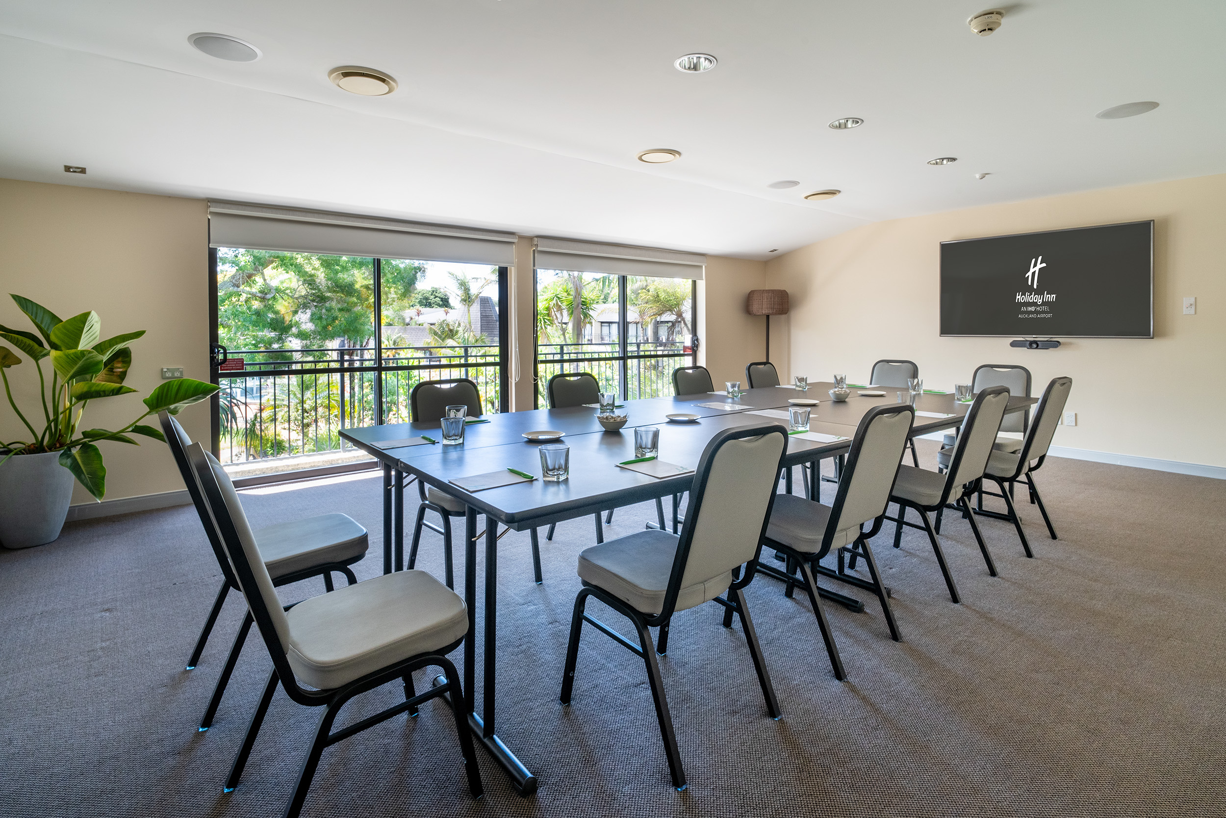 Small meeting room with a U-shaped table layout, wall-mounted screen, and garden-view windows