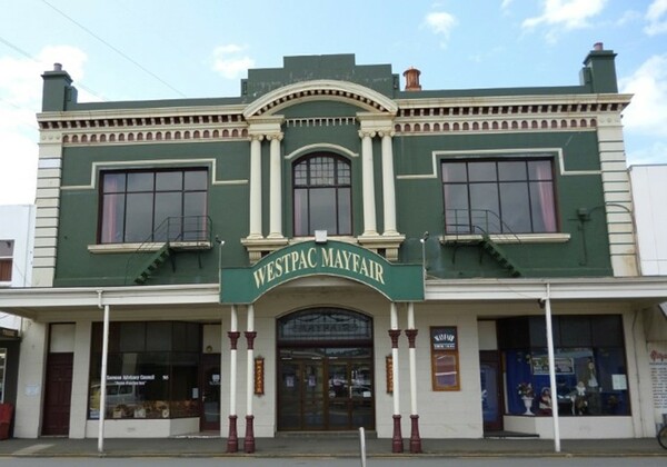 Two-storey green heritage commercial facade with white columns, arched windows, and ornate cornice