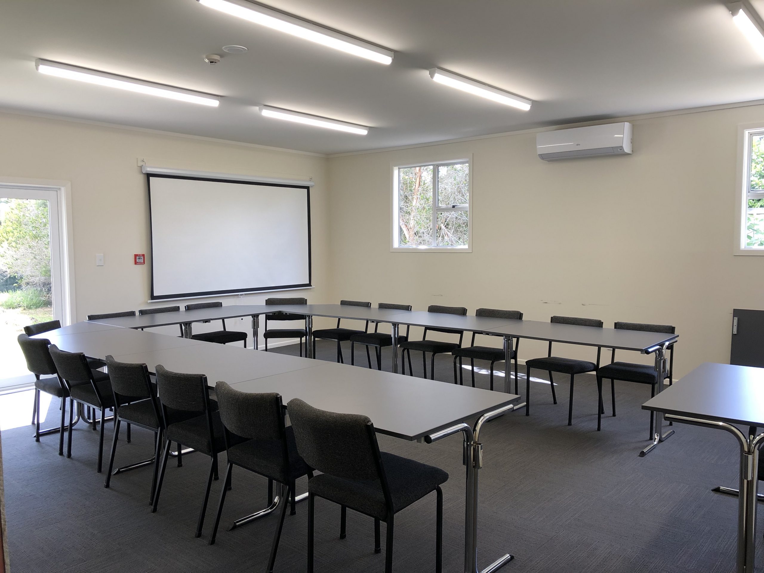 Plain meeting room with tables arranged in U-shape and projection screen