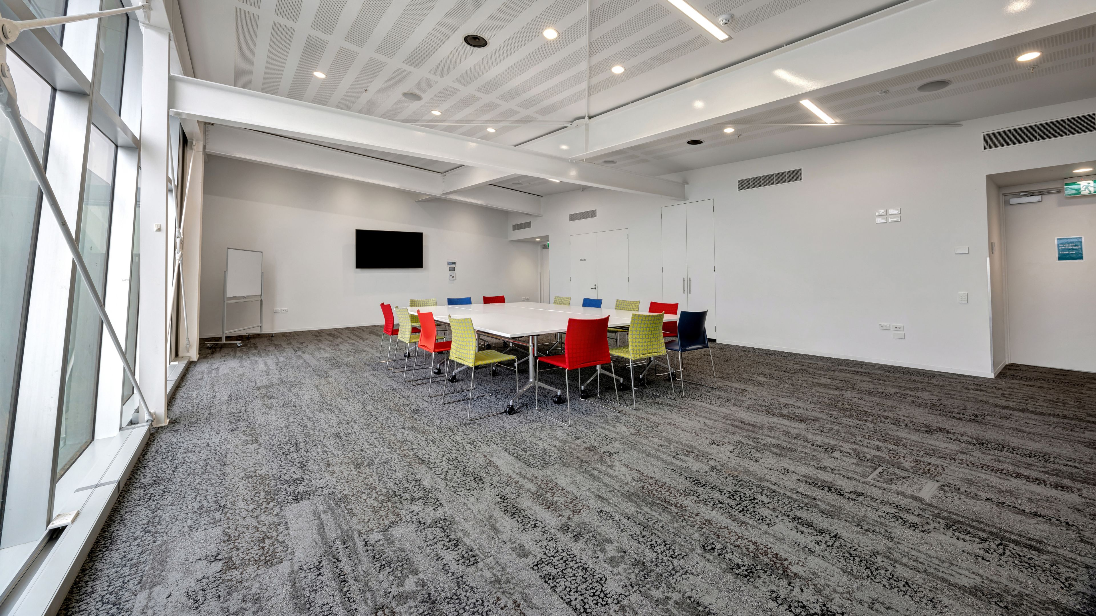 Meeting room with cluster of tables, coloured chairs and wall-mounted screen