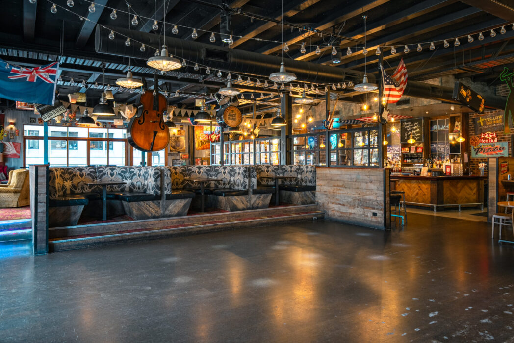Eclectic bar interior with exposed trusses, patterned booths, large cello hanging from ceiling and music memorabilia