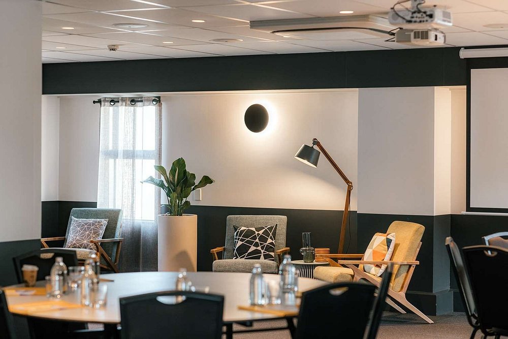 Modern breakout lounge with dark two-tone walls, mid-century chairs, floor lamp, and projector screen