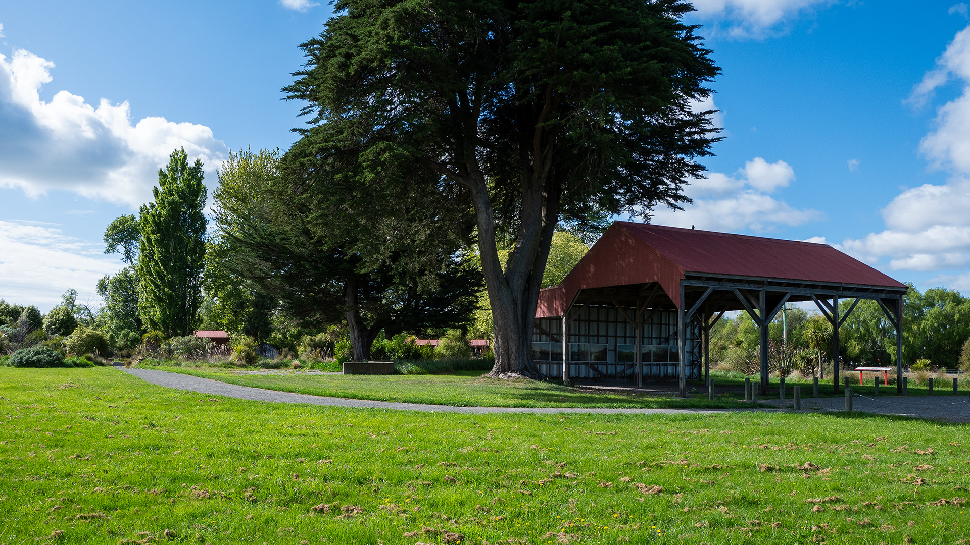 Open-sided picnic shelter with red roof beside trees in a park