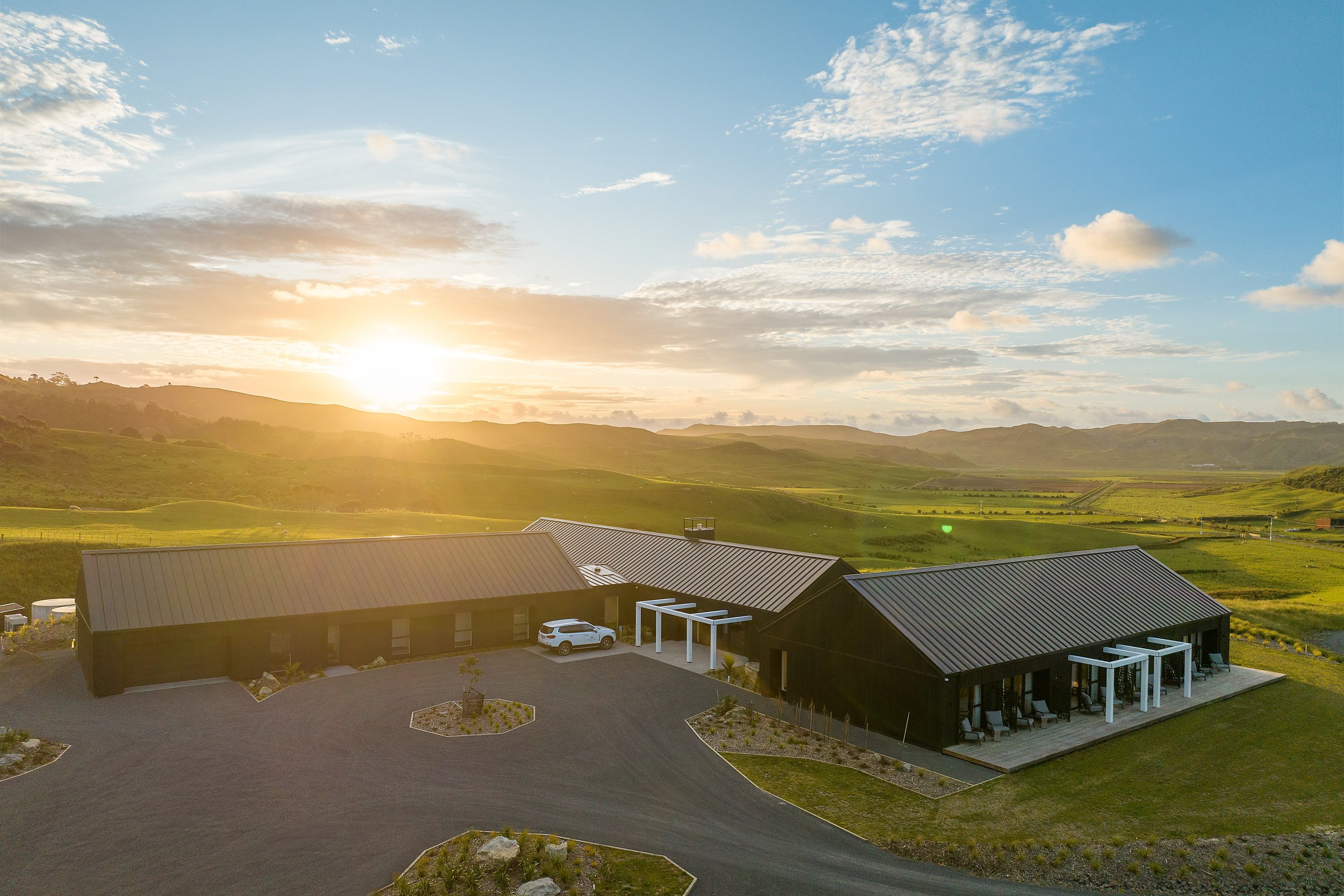 Aerial view of dark-clad barn-style buildings set on rolling green hills at sunset
