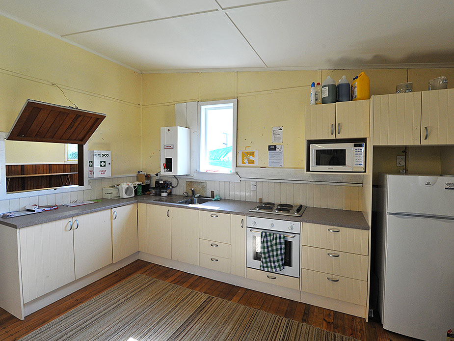 Plain kitchen with cream cabinetry, bench-top oven, microwave, and refrigerator, timber floor