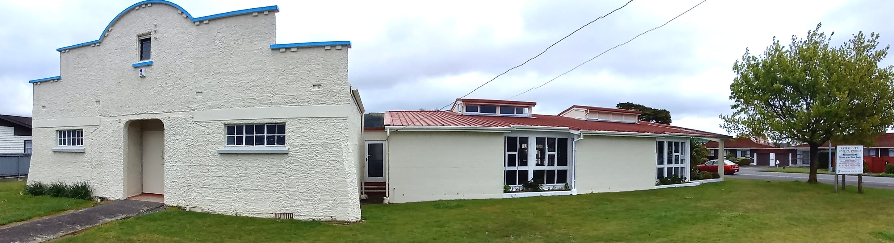 White rendered hall with stepped parapet and red-tiled roof wing, grassed surrounds