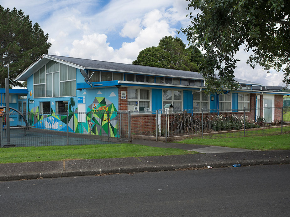 Single-storey blue community hall building with mural, fence and car park