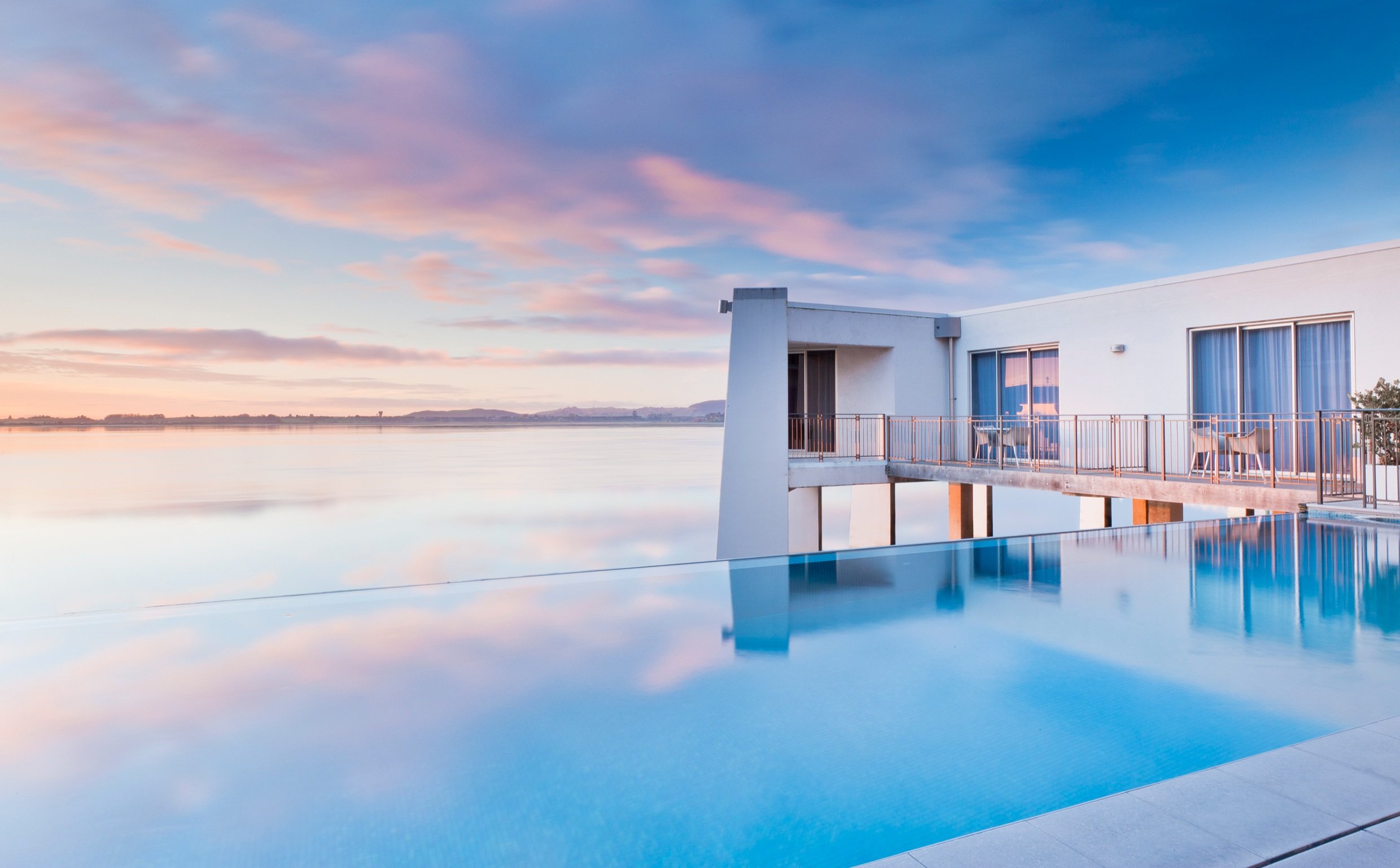 White render building with infinity pool at dusk, reflecting pink and blue sky over water