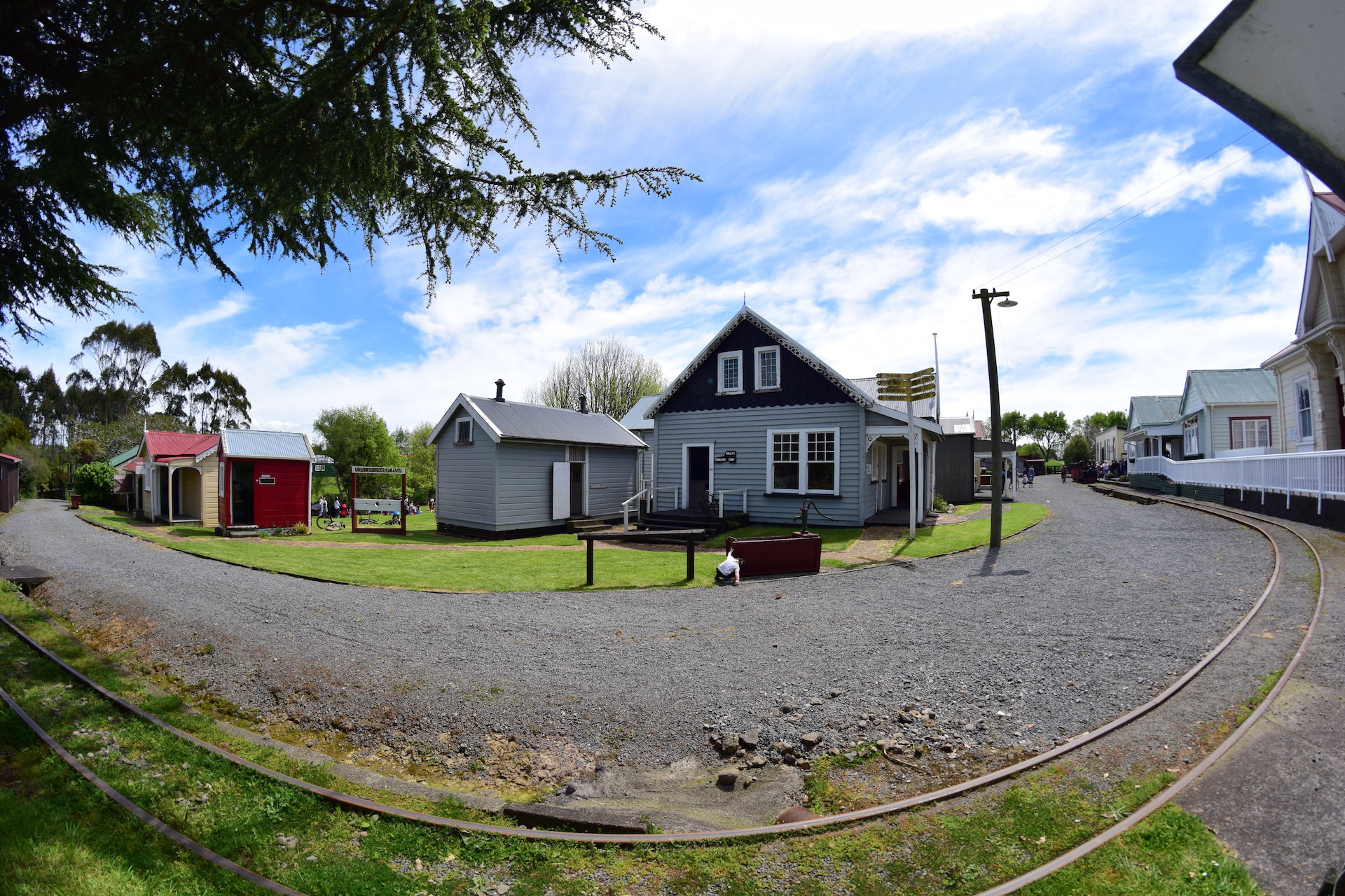 Open-air heritage village with weatherboard cottages, curved rail track, and gravel paths