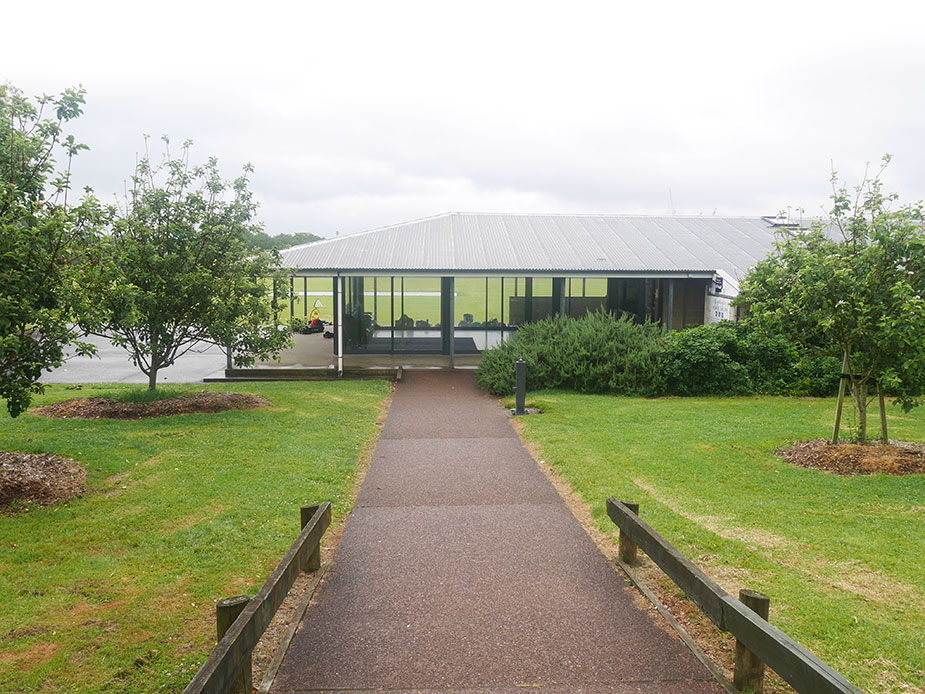 Low pavilion building beside cricket ground with pathway and trees