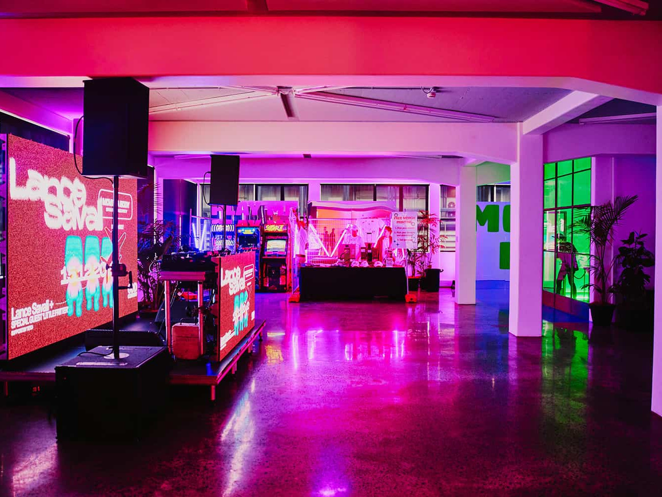 Open warehouse floor with polished concrete, coloured lighting, and DJ equipment