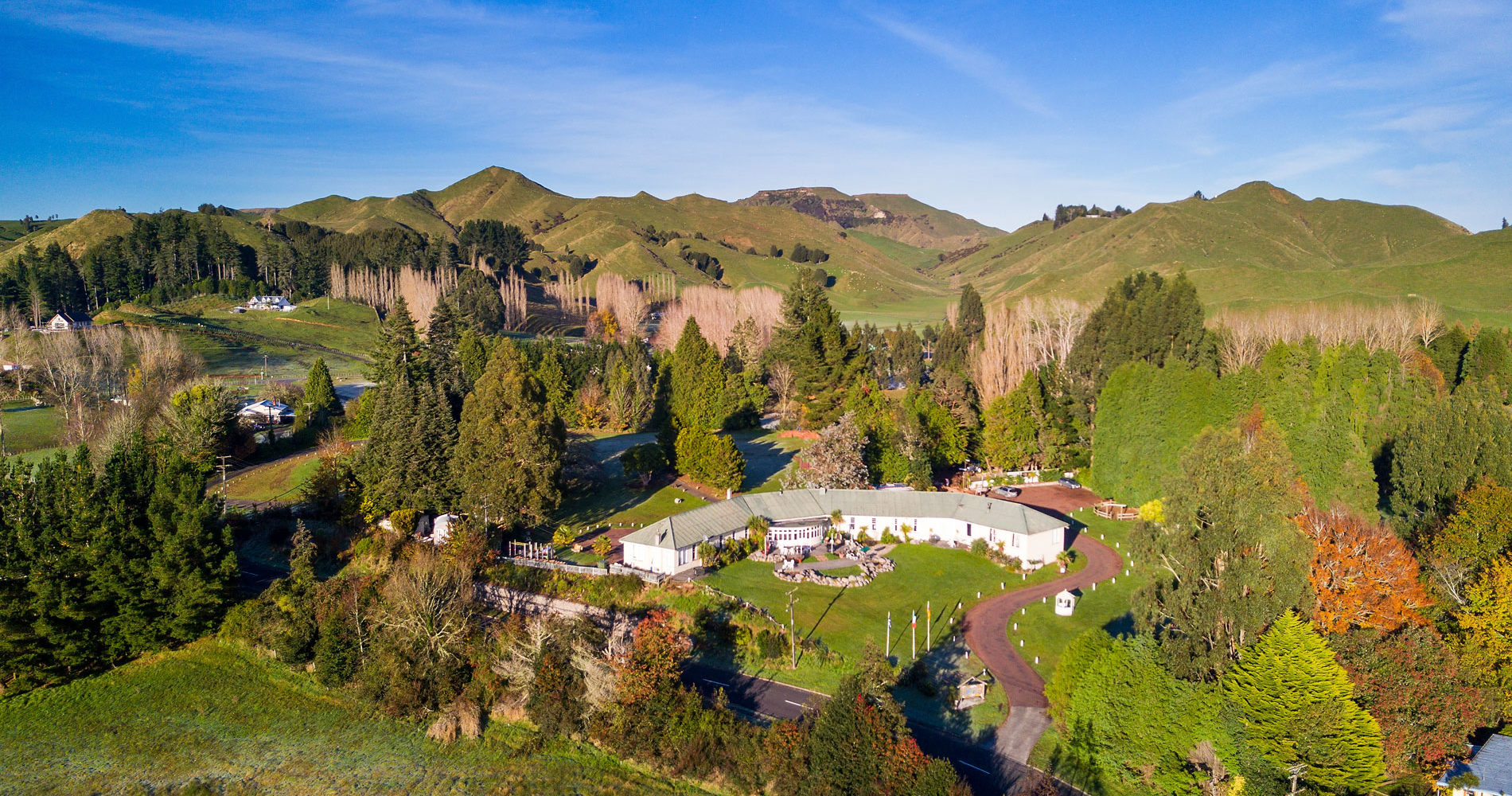 Aerial view of lodge buildings set among trees in a rural valley with hills
