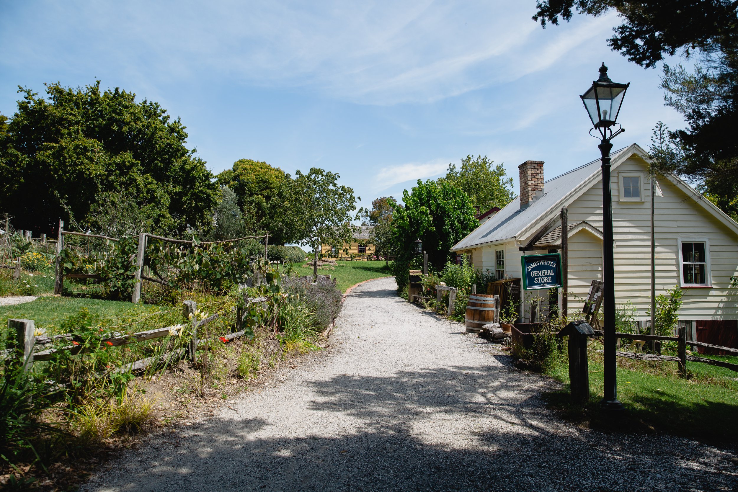 Gravel path through historical village with general store sign and period buildings