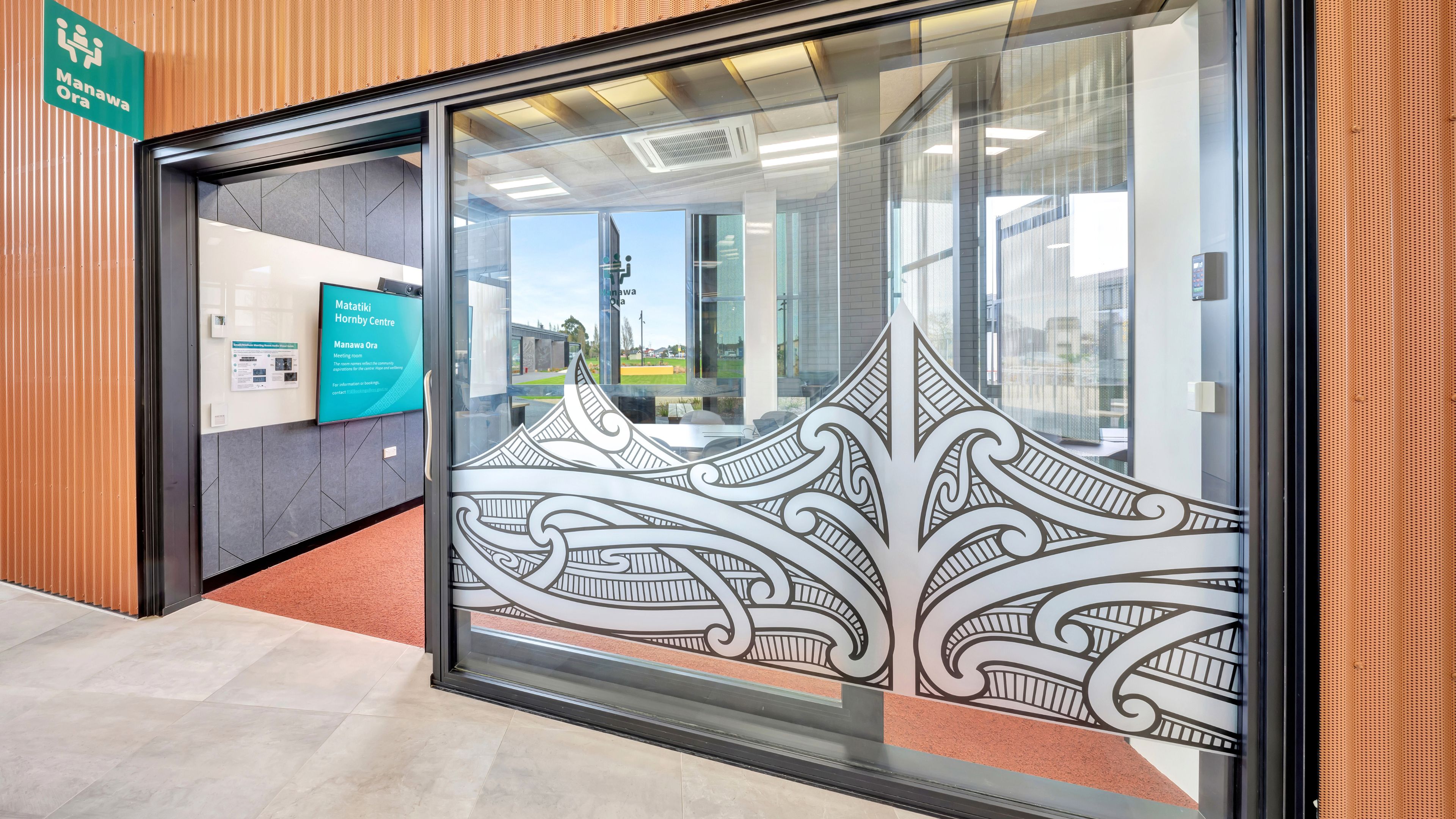 Glass entrance doors with decorative Māori-patterned etching on copper-clad building