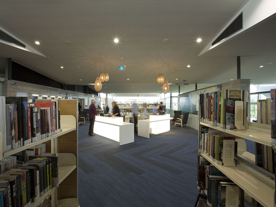 Open-plan library interior with bookshelves, pendant lights, and service desks