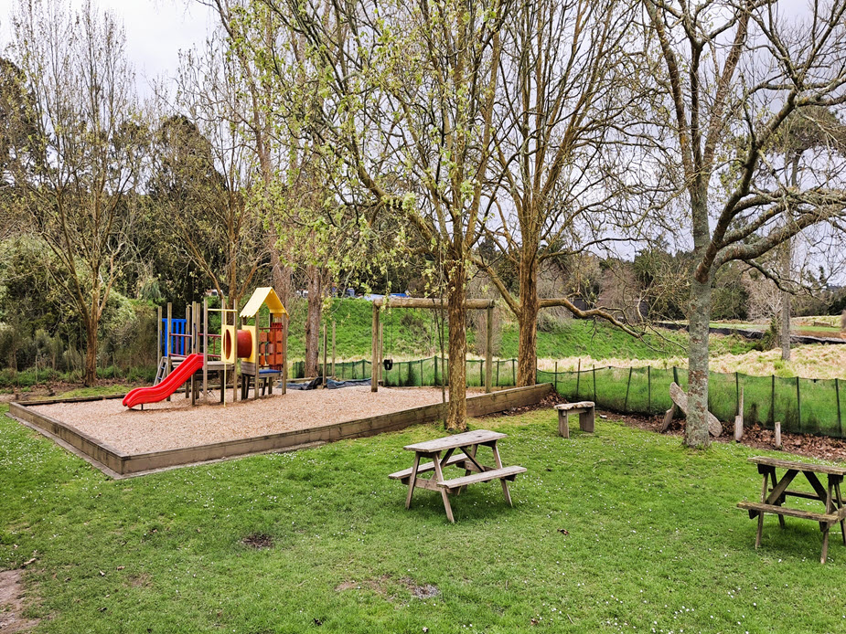 Outdoor playground with slide and climbing frame beside picnic tables and grass