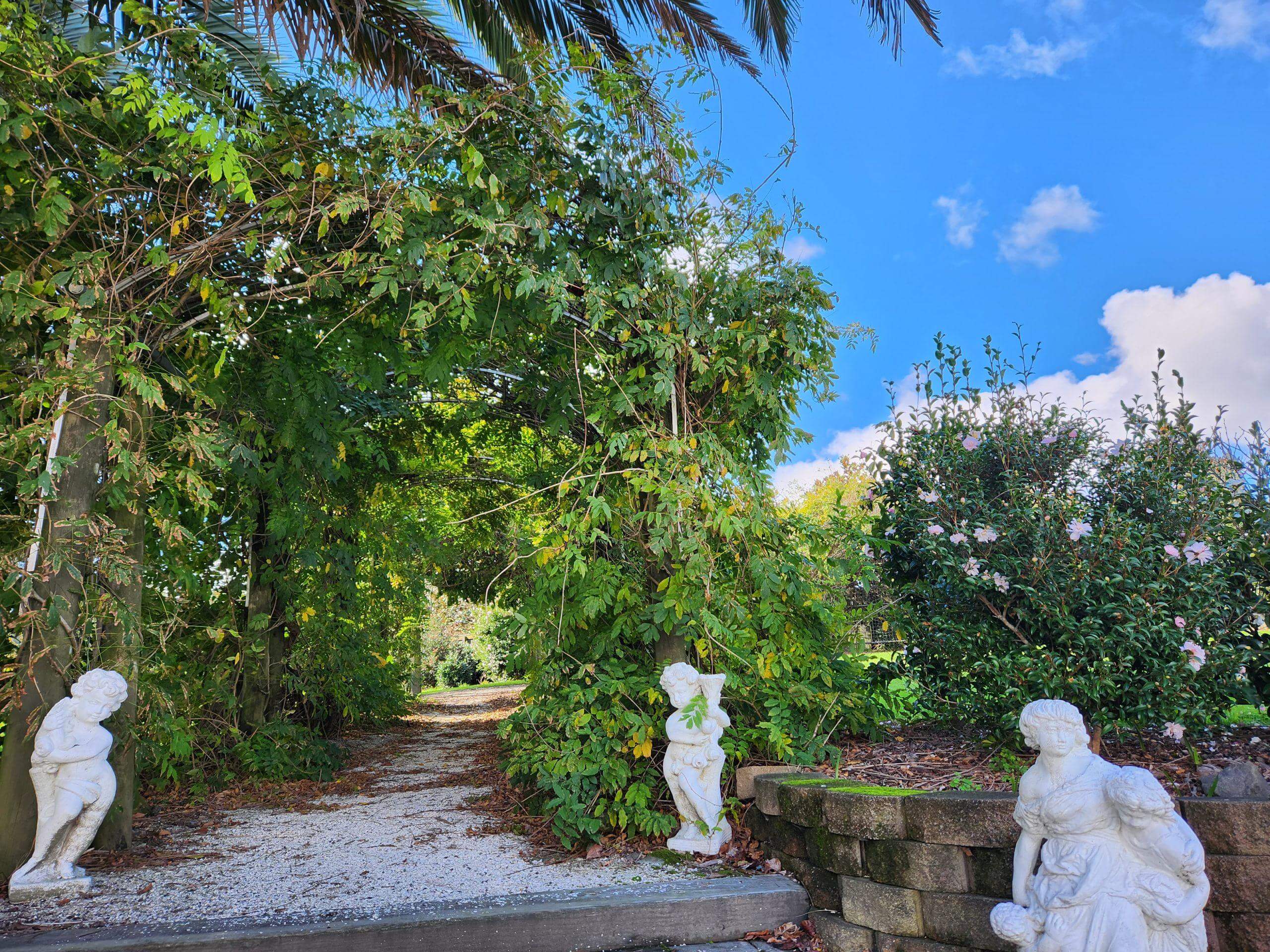 Garden path lined with classical stone statues leading through lush subtropical plantings